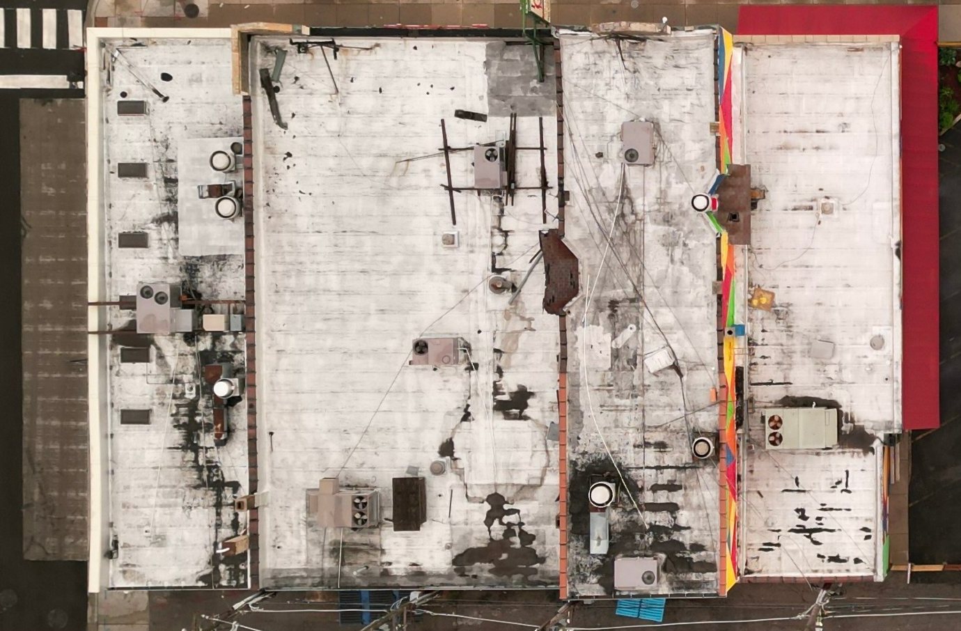 Overhead drone photo of a flat Chicago roof with dark rainwater staining, rooftop units and old equipment frames